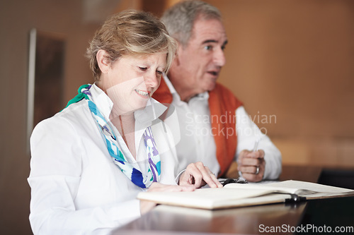 Image of Senior couple, reading and signing documents at hotel reception desk for booking, reservation or vacation. Mature man and woman filling forms, application or checking paperwork or sign in at resort