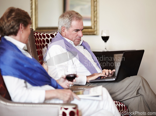 Image of Senior couple, laptop and typing on sofa in relax with wine for holiday, trip or reservation at hotel. Mature man working on laptop with woman enjoying accommodation service or lounge suite at resort