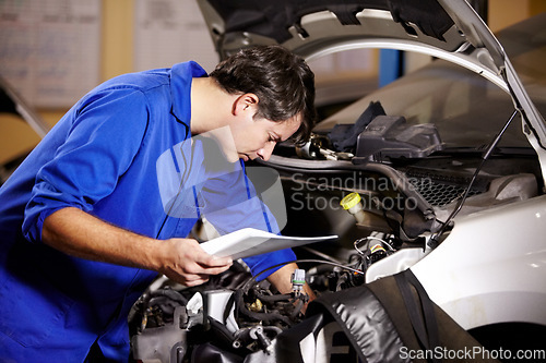 Image of Car, service and repair with a mechanic man in a workshop as an engineer looking at the engine of a vehicle. Garage, report or quote with a young technician working under the hood of an automobile