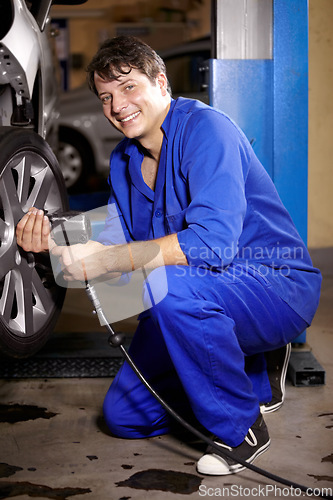 Image of Mechanic, man and smile by wheel in shop, electric drill and car service or repairs for maintenance. Technician, male person and tire change for automobile, rim and vehicle inspection in portrait