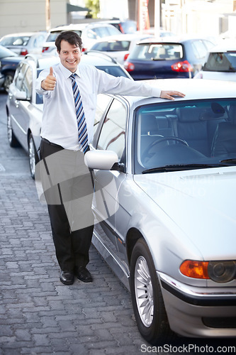 Image of Portrait, thumbs up and a man at the dealership for a car sale, lease or rental in a commercial parking lot. Smile, retail or agreement with a happy young salesman working in the vehicle trade