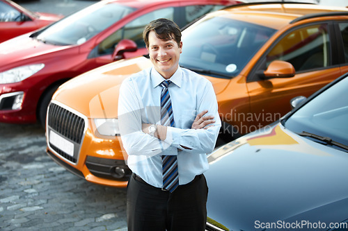 Image of Portrait, smile and a man arms crossed at a dealership for car sale in a commercial parking lot. Business, luxury and automobile trade with a happy young salesman outdoor for transport service