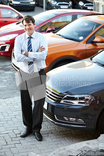 Image of Portrait, smile and a man arms crossed in a parking lot for car sale at a commercial dealership. Business, luxury and automobile trade with a happy young salesman outdoor for transport rental