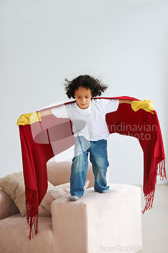 Image of Jump, children and a boy superhero in a costume on a sofa in the living room of his home for playing a game. Flying, growth and fantasy with a young kid in a cape for justice or safety cosplay