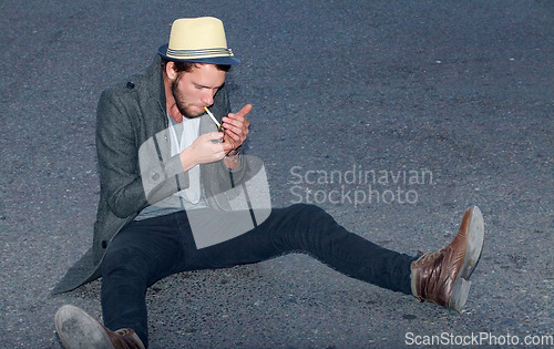 Image of Hipster, man and sitting in road with cigarette for smoking, fashion or experience outdoor on ground. Person, smoke and street for adventure, travel or downtown with tobacco, light and confidence