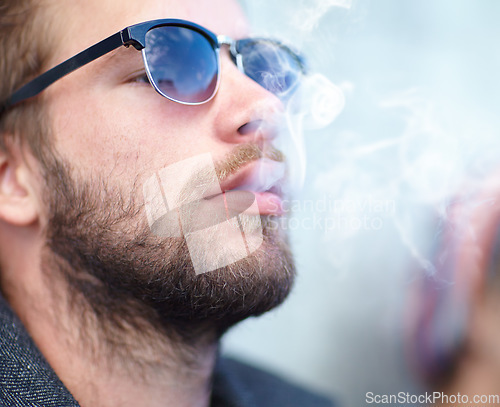 Image of Face, man and smoking with sunglasses for experience, fun and cigarette enjoyment outdoor. Person, hipster and guy with smoke for exhale, serious and smoker with tobacco satisfaction and shades