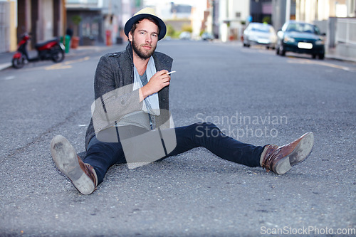 Image of Portrait, outdoor and man smoking, fashion on the ground and relax with trendy clothes, New York and stylish. Person, outdoor and guy with cigarette, tobacco and smoke with casual, outfit and city