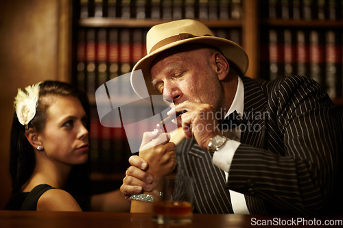 Image of Mafia, boss and man with cigarette in office, woman and light for smoking. Mature person, godfather and hat in suit for power, reputation and career for criminal activity with tobacco for relaxation