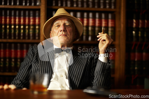 Image of Portrait, mafia and boss with cigarette in office for habit, smoking or relaxing by desk. Mature, mob leader and retro fashion in suit, bowtie and hat for crime, danger or power with vintage look