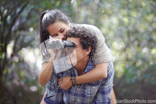 Image of Man, woman and piggyback in forest with binocular for travel, adventure or sightseeing in nature with happiness. Couple, people and tourist hiking outdoor in woods for experience, holiday or vacation