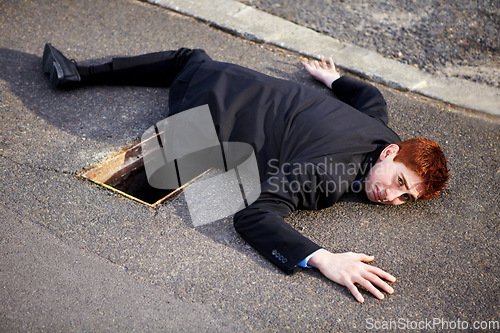 Image of Portrait, accident and an unlucky business man on a street in the city after falling into a hole. Mistake, stuck or clumsy and a ginger corporate professional on the road in a suit with a problem