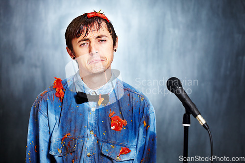 Image of Portrait, sad and a man comic in tomato with a microphone after a bad performance at a comedy club. Depression, fail or boo with an unhappy young comedian in studio on a gray background for a show