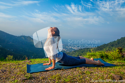 Image of Woman practices yoga asana Urdhva Mukha Svanasana outdoors