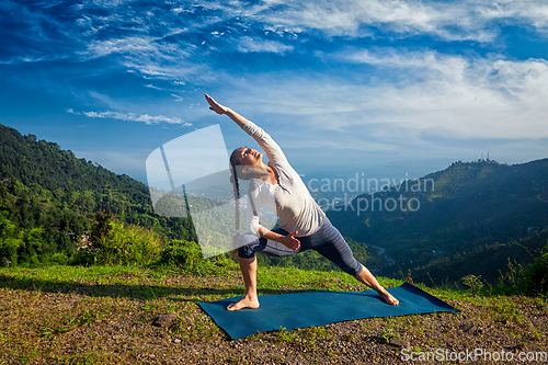 Image of Woman practices yoga asana Utthita Parsvakonasana outdoors