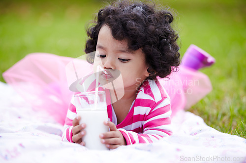 Image of Kid, girl and lying on grass with milk for drinking by straw in pink tutu, princess or dress up. Child, youth and curly hair with calcium for development, growth and strong bones with healthy diet