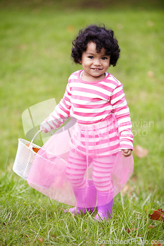 Image of Portrait, happy child and tutu on grass in park with basket for leaves for autumn. Little girl, pink clothes and curly hair with rain boots for growth, development and changing of season for Easter
