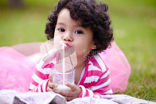 Image of Portrait, child and glass of milk on grass while lying down with satisfaction on face for beverage. Little girl, pink tutu and curly hair for development for health, nutrition and calcium for growth