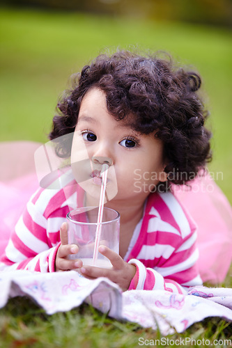 Image of Portrait, child and drinking of milk on grass for nutrition, calcium and bone development on picnic. Youth, curly hair and girl in pink tutu for lactose beverage for balanced diet, health and lawn