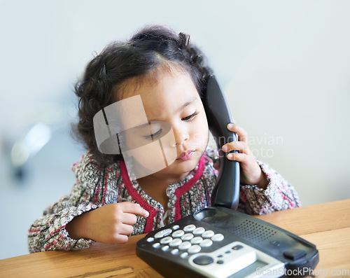 Image of Playing, serious and a child on a telephone phone call for communication in a house. Home, contact and a girl, kid or baby listening on a landline for conversation, play or a discussion at a desk