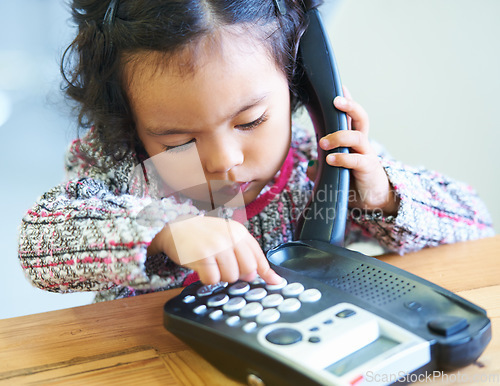 Image of Playing, dial and a child on a telephone phone call for communication in a house. Home, contact and a girl, kid or baby speaking on a landline for conversation, play or a discussion at a desk