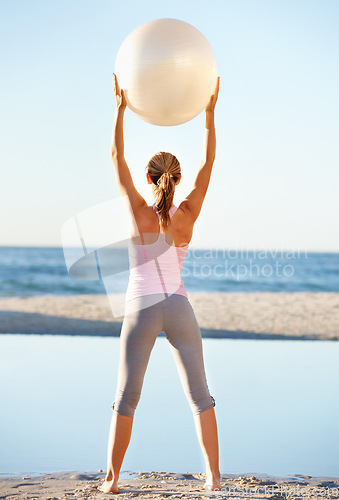 Image of Woman, hold and pilates ball for fitness on beach by stretching for balance in wellness with back view. Female person, yoga and movement in nature for peace, calm or zen in prepare for workout