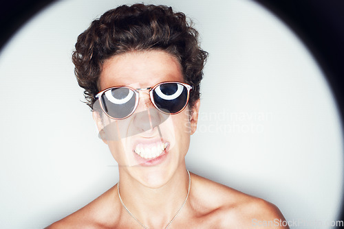 Image of Man, sunglasses and spotlight for studio portrait, fashion or shirtless with edgy punk style by background. Person, teeth and unique with halo for confidence, attitude or jewelry for trendy aesthetic