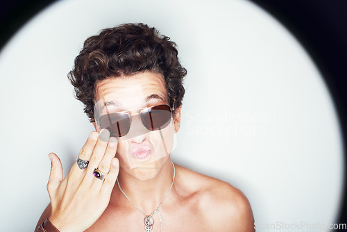 Image of Man, sunglasses and pout in studio spotlight for fashion, shirtless and edgy punk style by white background. Rock person, halo and hand for kiss with confidence, attitude and jewelry for aesthetic