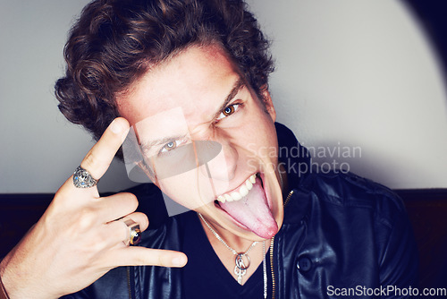 Image of Rockstar man, horns and hand in studio for emoji in spotlight, fashion or leather jacket by background. Person, symbol and icon by halo for portrait, punk style and tongue with jewelry for aesthetic