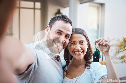 Image of Young caucasian couple taking a selfie holding house keys. Happy couple moving into their house. Smiling couple taking a photo outside before moving into their first real estate purchase