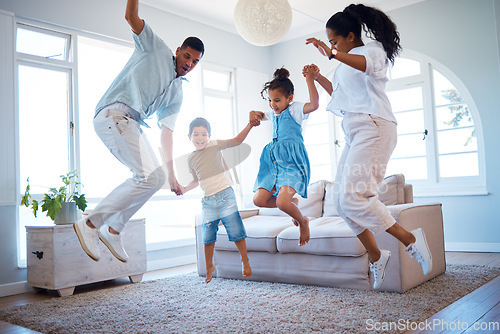 Image of Young parents jumping and playing with their two children at home. Happy hispanic family having fun spending time together. Little boy and girl holding hands and jumping in the air with mom and dad