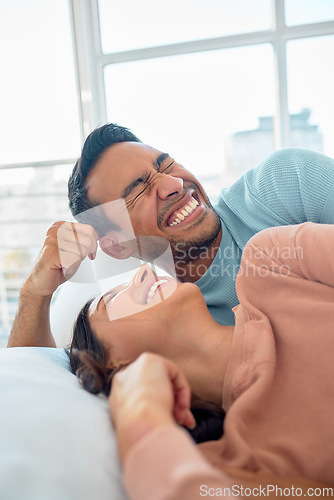 Image of Happy young mixed race couple in a loving relationship laughing while relaxing together in bed at home. Boyfriend making a silly face while telling funny and lighthearted jokes to cheerful girlfriend