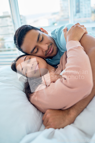 Image of Young mixed race couple lying in bed together and cuddling early in the morning. Handsome asian man holding his beautiful hispanic wife while he sleeps at home. Feeling safe and protected in his arms