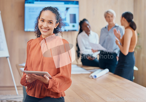 Image of Young mixed race businesswoman with curly hair holding and working on a digital tablet while standing in a meeting at work. One hispanic female boss smiling while using a digital tablet in a boardroo