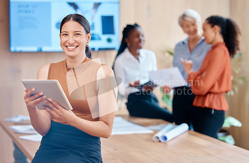 Image of Beautiful young mixed race business woman using a tablet while leaning against the boardroom table after a meeting with her female only colleagues in the background. Our office is going digital