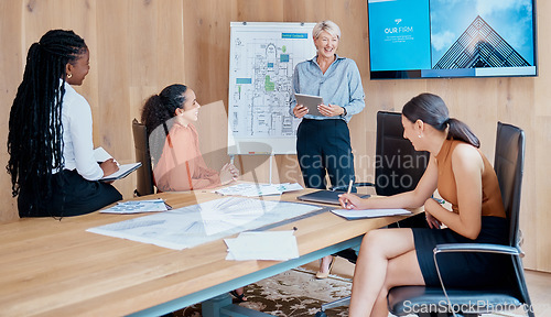 Image of Mature caucasian businesswoman smiling and standing using a tablet while giving a presentation in the boardroom during a meeting with her female only diverse multiracial colleagues in a workplace. Ou