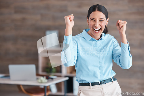 Image of Young happy mixed race businesswoman standing and cheering with her fists alone in an office at work. One hispanic businesswoman celebrating success and victory at work