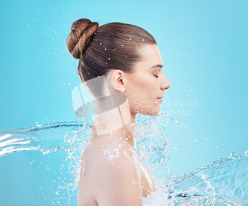 Image of Its amazing what a shower does. a beautiful young woman being splashed with water against a blue background.