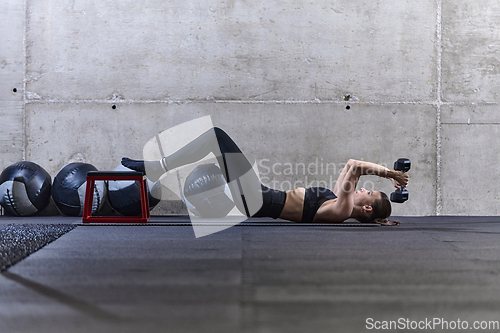 Image of A fit woman is lying on the gym floor, performing arm exercises with dumbbells and showcasing her dedication and strength.