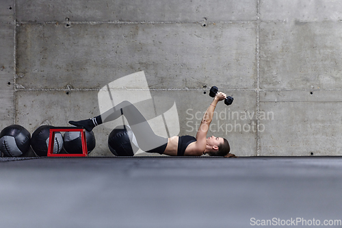 Image of A fit woman is lying on the gym floor, performing arm exercises with dumbbells and showcasing her dedication and strength.