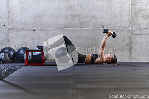 Image of A fit woman is lying on the gym floor, performing arm exercises with dumbbells and showcasing her dedication and strength.