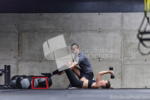 Image of A muscular man assisting a fit woman in a modern gym as they engage in various body exercises and muscle stretches, showcasing their dedication to fitness and benefiting from teamwork and support