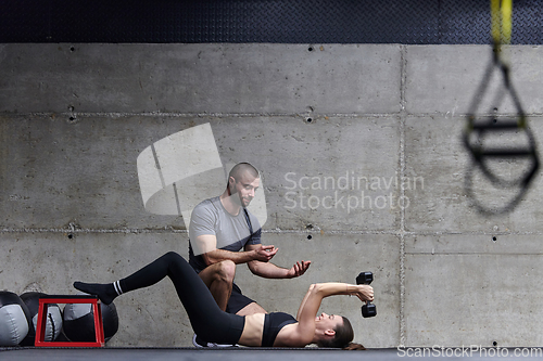 Image of A muscular man assisting a fit woman in a modern gym as they engage in various body exercises and muscle stretches, showcasing their dedication to fitness and benefiting from teamwork and support