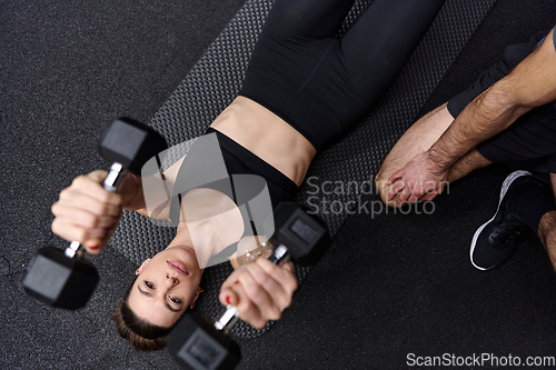 Image of A muscular man assisting a fit woman in a modern gym as they engage in various body exercises and muscle stretches, showcasing their dedication to fitness and benefiting from teamwork and support