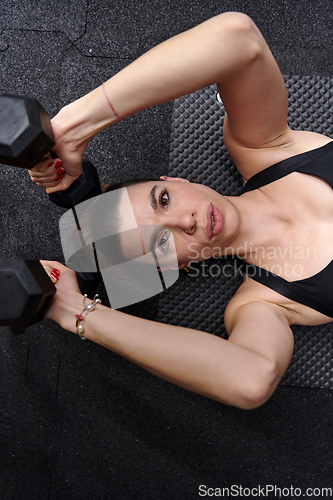 Image of A fit woman is lying on the gym floor, performing arm exercises with dumbbells and showcasing her dedication and strength.