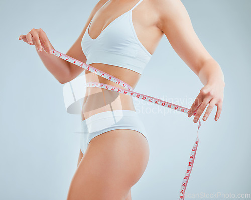 Image of Struggling to keep the weight off. a woman holding a measuring tape around her waist.