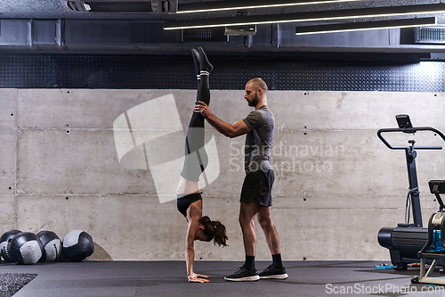 Image of A muscular man assisting a fit woman in a modern gym as they engage in various body exercises and muscle stretches, showcasing their dedication to fitness and benefiting from teamwork and support