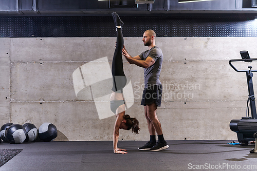 Image of A muscular man assisting a fit woman in a modern gym as they engage in various body exercises and muscle stretches, showcasing their dedication to fitness and benefiting from teamwork and support