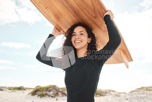 Image of You can take a surfer out of the surf. an attractive young woman carrying a surfboard at the beach.