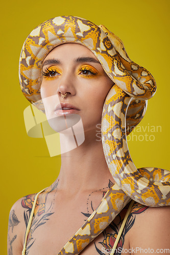 Image of In a golden state of mind. a young woman posing with a snake on her head against a yellow background.