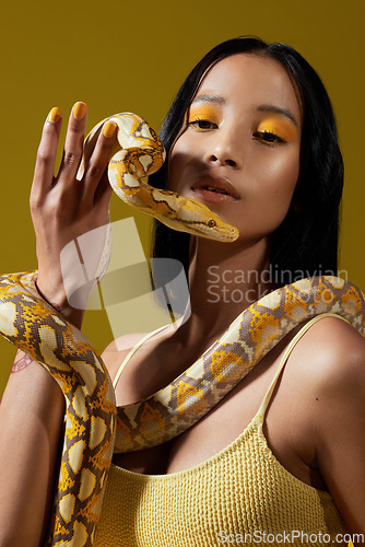 Image of Live life in warm yellows. a young woman posing with a snake around her neck against a yellow background.